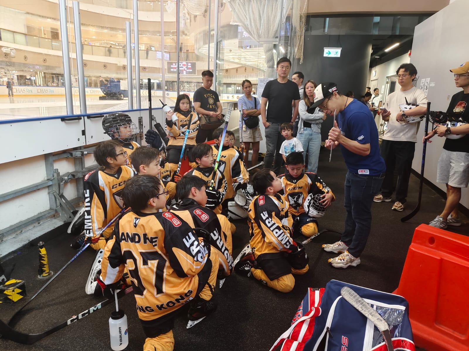 A coach going through a drill with kneeling Empire players rinkside