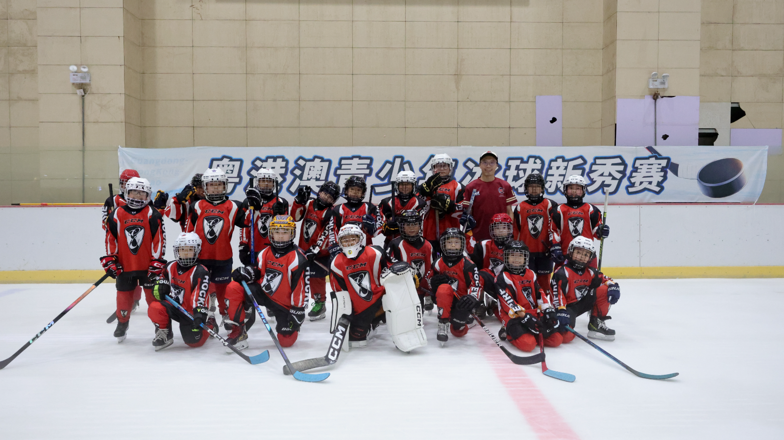 Empire Glory players and coach on the ice in front of the Guangdong–Hong Kong–Macao Youth Ice Hockey Rookie Tournament banner in Zhuhai